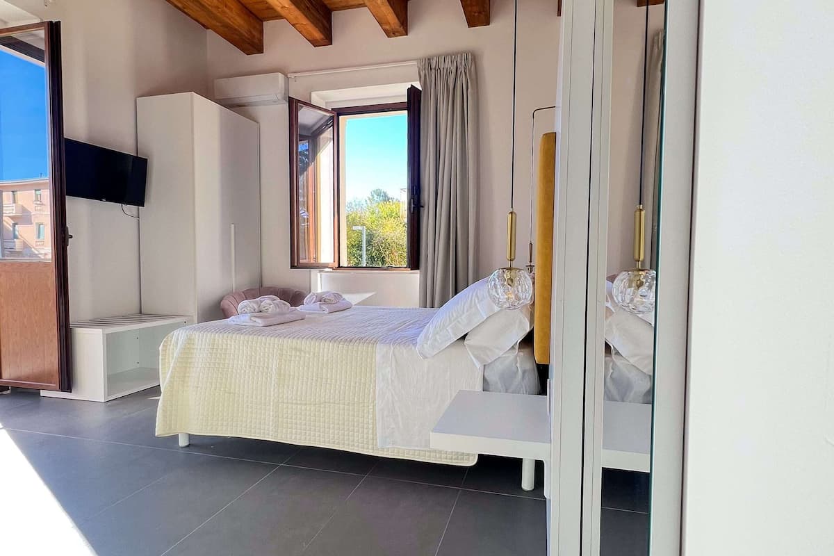 A bedroom with a bed, a TV, a window with curtains, and a balcony.