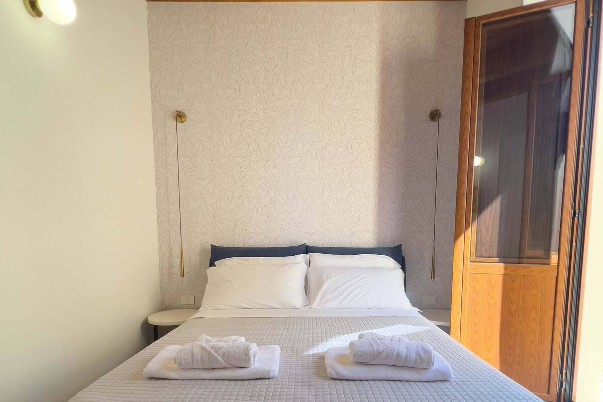 A neatly made bed with two towels, a wooden ceiling, and a wardrobe with a glass door.