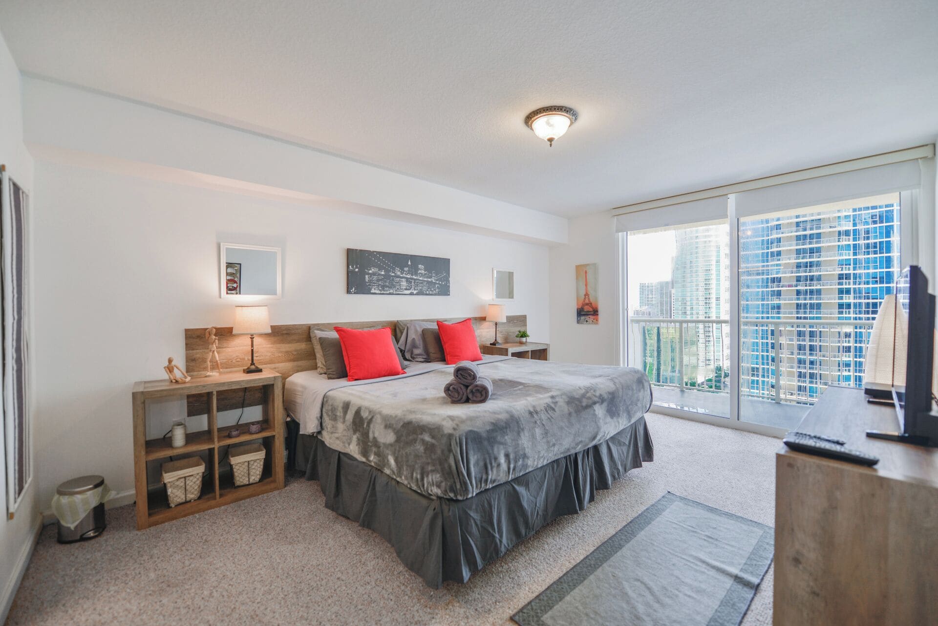 Ein modernes Schlafzimmer mit einem großen Bett, Nachttischen, einem Holznachtkästchen und Blick auf die Stadt durch große Fenster.
