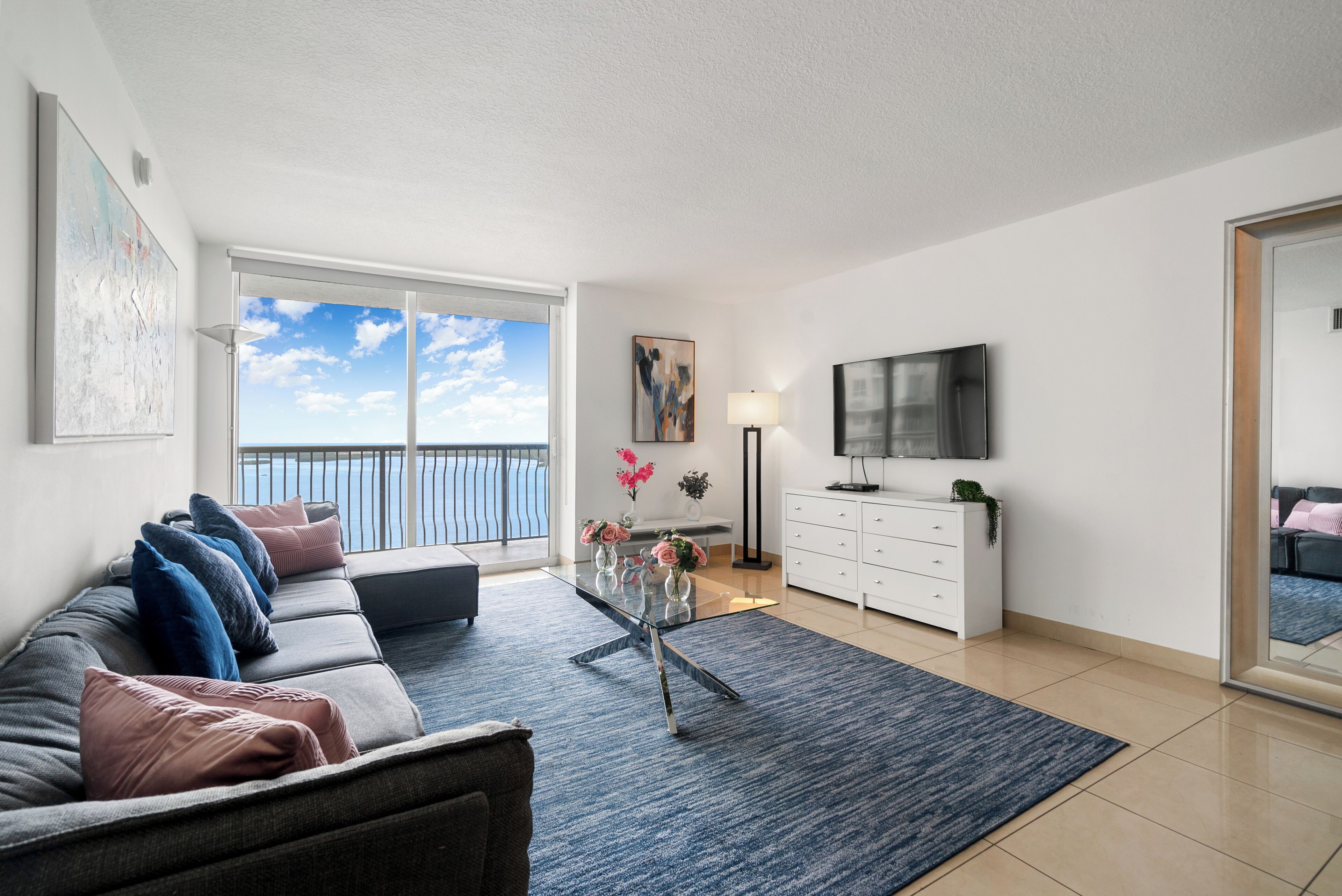 A modern living room with a sofa, coffee table, and a view of the sea through large windows.