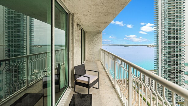 Ein Balkon mit Stuhl, Tisch und Blick auf das Meer und Gebäude.