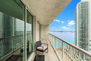 A balcony with a chair, a table, and a view of the sea and buildings. - Brickell Condo - Waterfront walks - We Host (Miami)