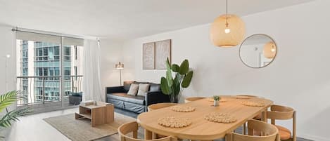 A modern living room with a dining area, large windows, and a view of the cityscape.