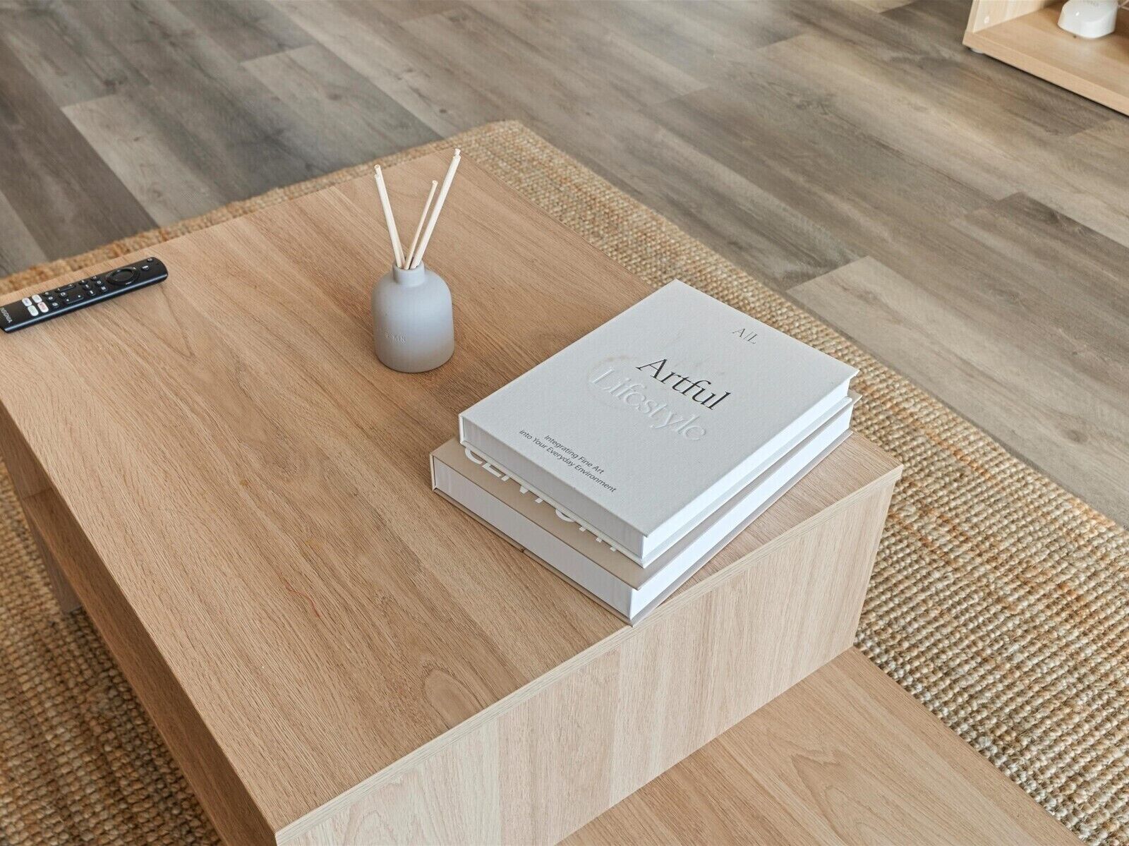 A wooden coffee table with a remote control, a reed diffuser, and a book titled 'Artful Lifestyle.'