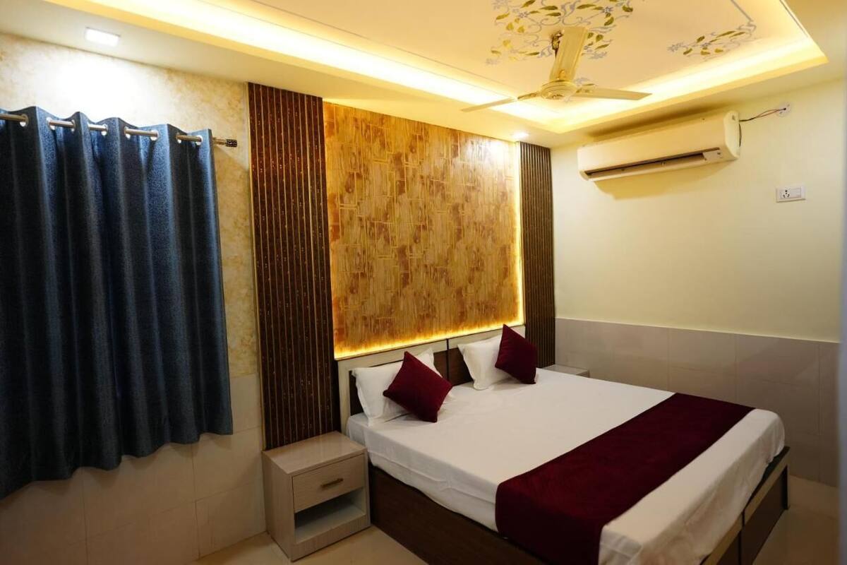 A hotel room with a bed, a nightstand, a wall-mounted air conditioner, and a ceiling fan.