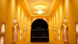 A corridor with a large ornate door, arched windows, and a chandelier. - Aashirwad Haveli (Sawai Madhopur)