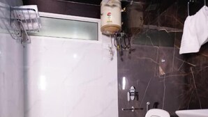 A bathroom with a white toilet, a shower area, and a marble wall. - Aashirwad Haveli (Sawai Madhopur)