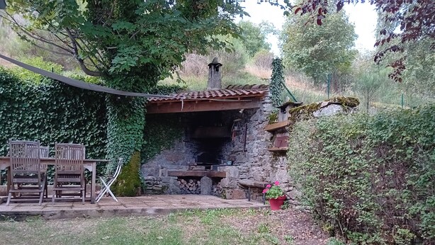 A rustic outdoor kitchen with a stone chimney, wooden chairs, and a potted plant. - House and garden for 6 people near lakes and hiking trails (Luc)