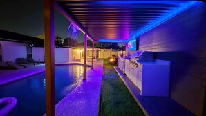 A poolside area with a covered patio, a barbecue grill, and a seating area with lounge chairs.