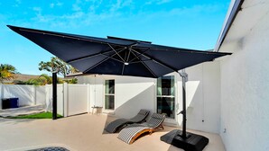 A backyard with a swimming pool, two lounge chairs, a large umbrella, and a white fence.