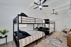 Een slaapkamer met een stapelbed, een ventilator aan het plafond, een kleine tafel met een plant en een stoel.