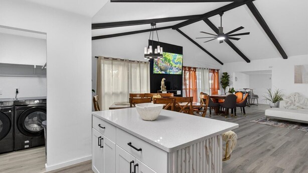 A modern kitchen with built-in appliances, a dining area with a large island, and a living room with a sofa and a TV.
