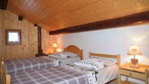 Un dormitorio de cabaña de madera con dos camas, una mesita de noche con lámpara y una ventana con cortina.