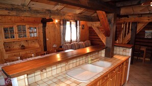 Interior de una cabaña de madera con cocina que incluye una isla grande con fregadero y comedor con banco y sillas.