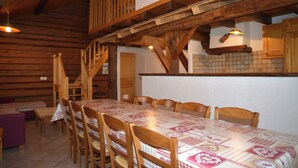 Un comedor de madera con una mesa larga y sillas, una escalera y una zona de cocina con armarios de madera.