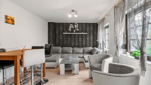 Een moderne woonkamer met een modulaire bank, een eettafel met barkrukken, een salontafel en een groot raam met gordijnen.