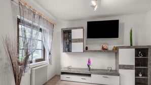 Een moderne woonkamer met een grote flatscreen televisie, een ingebouwde entertainmentkast met planken en een decoratieve vaas.