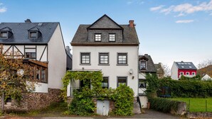 Een traditioneel Europees huis met een steil dak, meerdere ramen en een stenen muur.