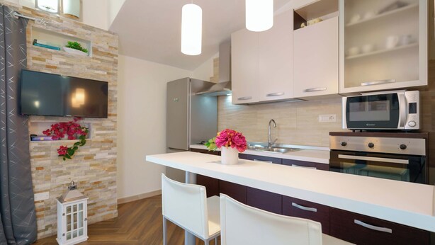 Una cocina moderna con encimera blanca, electrodomésticos de acero inoxidable y un televisor empotrado.