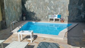 Zona de piscina con paredes de piedra, una escalera, sillas de descanso y una pequeña mesa con un adorno de pez.