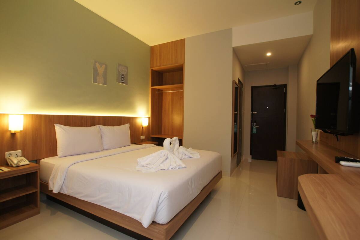 Quarto de hotel com cama, mesa de cabeceira com telefone, televisão, guarda-roupa de madeira e escrivaninha com cadeira.