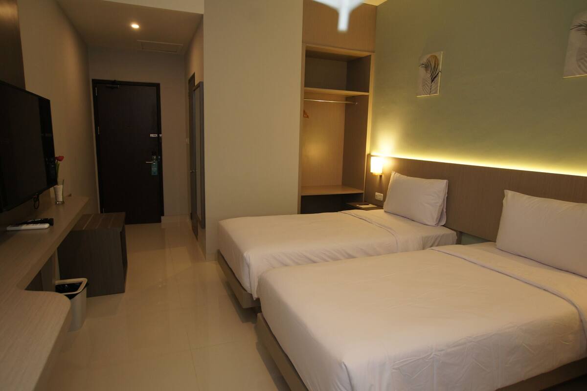 Quarto de hotel com duas camas, televisão, secretária e armário.