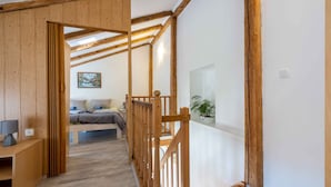 Ein Zimmer mit Holzboden, einem Bett mit grauer Decke, einem Nachttisch mit Lampe und einer kleinen Pflanze auf einem Regal.