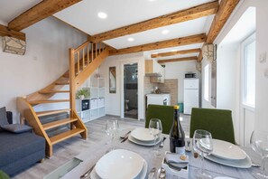 Comedor con escalera de madera, cocina al fondo y una mesa para dos, con copas de vino y platos.