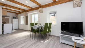 Eine moderne Küche mit Holzbalken, einem Essbereich mit grünen Stühlen, einem Fernseher auf einem Standfuß und einem kleinen Tisch mit einer Fernbedienung.