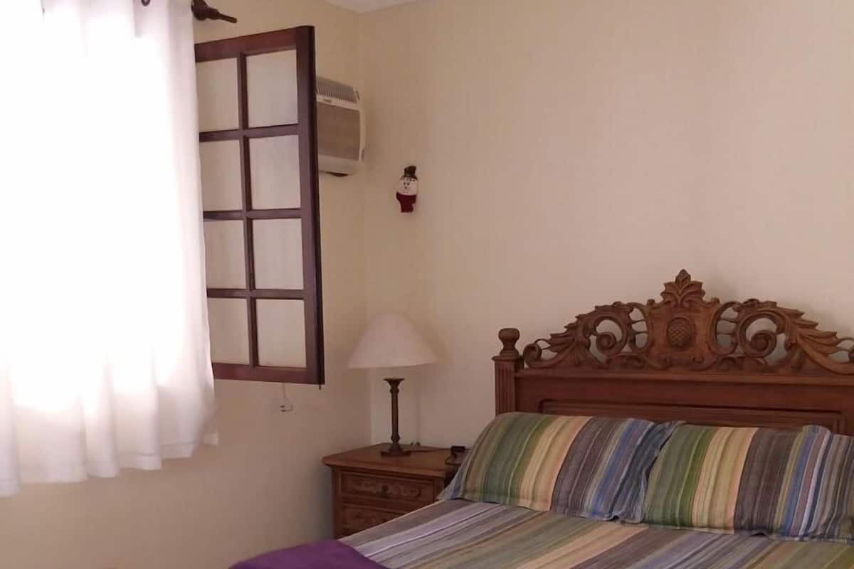 A wooden bed with a headboard, a nightstand with a lamp, and a window with curtains.