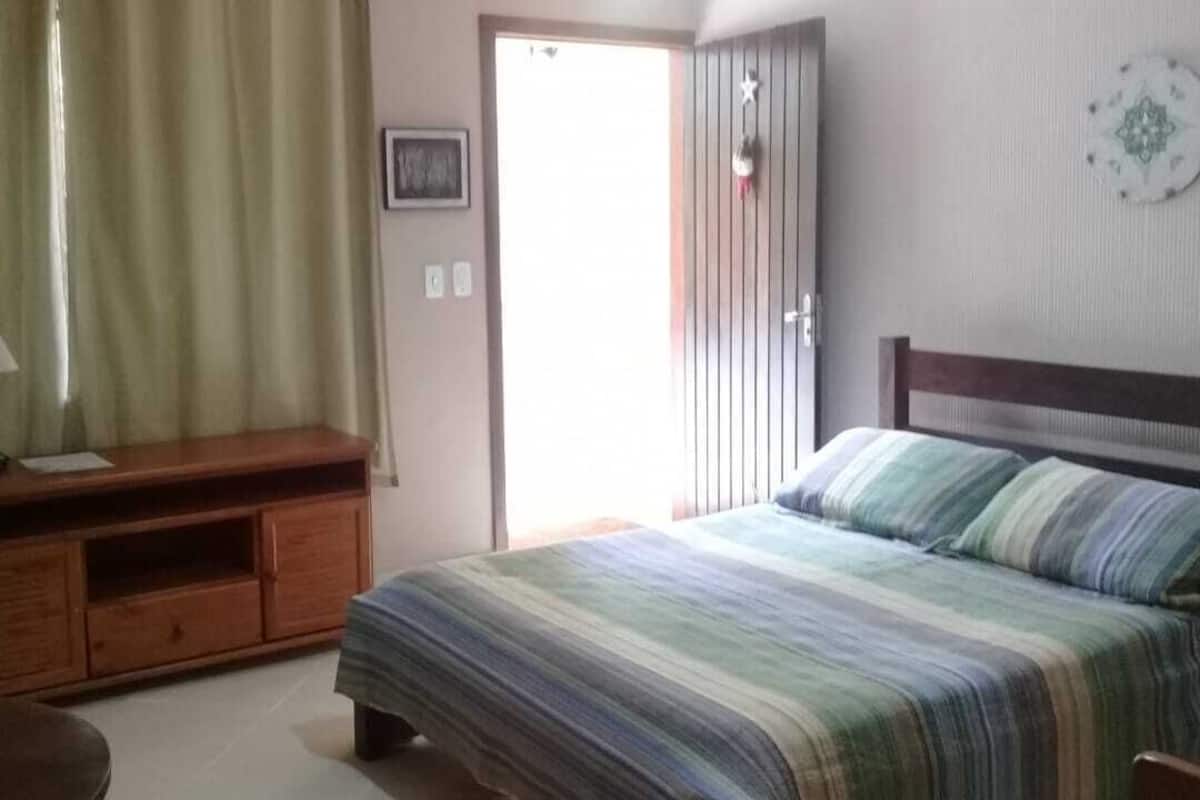 A bedroom with a bed, a wooden nightstand, a lamp, and a door leading to another room.