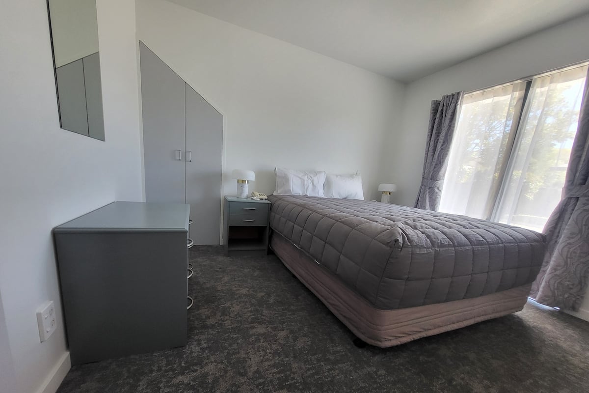A bedroom with a bed, bedside tables, a desk, a mirror, and a window with curtains.