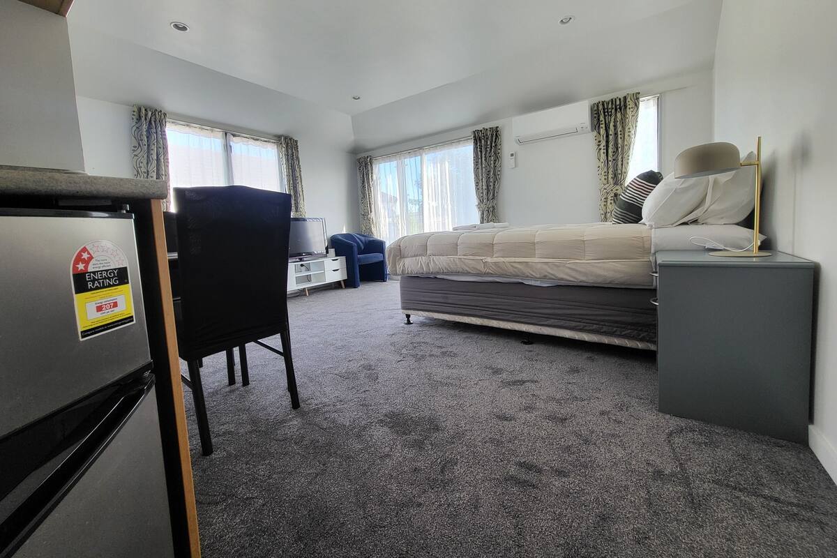 A hotel room with a bed, a desk, a chair, a TV, and a small fridge.