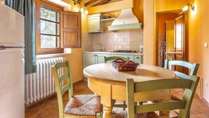 A kitchen with a round table, chairs, a refrigerator, cabinets, a window, and a radiator. - Holiday apartment with air conditioning and pool (Sorano)