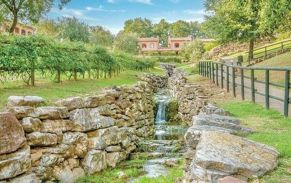 A stone-lined stream with a waterfall, surrounded by lush greenery and a stone fence.
