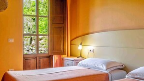 Una habitación con dos camas, una ventana con vista a vegetación, una mesita de noche con lámpara y paneles de madera.