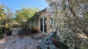 A stone-paved patio with a small seating area, a glass door entrance, and surrounding lush vegetation.