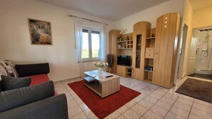 Un salon comprenant un canapé, une table basse, un téléviseur et un meuble en bois avec des étagères.