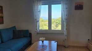Ein Zimmer mit einem blauen Sofa, einem Tisch mit Blumenvase und einem mit Vorhängen drapierten Fenster.