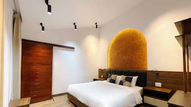 Une chambre moderne dotée d’un grand lit, de parquet, d’une arche murale originale et de spots encastrés au plafond.