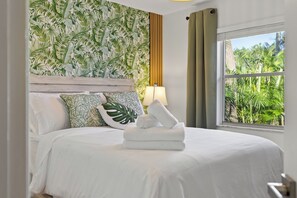 Ein Hotelzimmer mit Bett, tropischem Wanddesign, einem Fenster mit Blick auf Grünflächen und einer Holzvertäfelung.