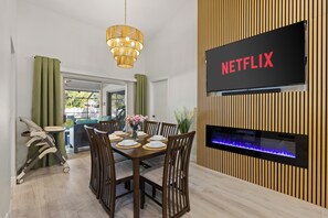 Ein moderner Essbereich mit einem Holztisch, gedeckt für sechs Personen, einem an einer Holzwand montierten Fernseher und einem Kamin darunter.