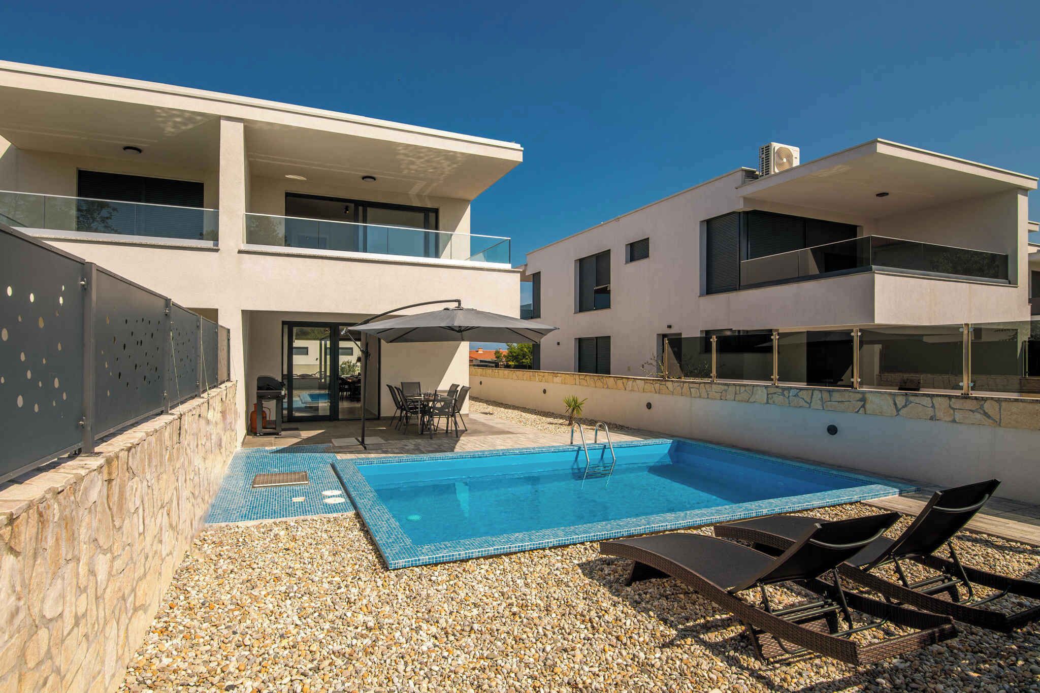 Un edificio moderno de dos pisos con piscina, asientos exteriores y un muro de piedra.