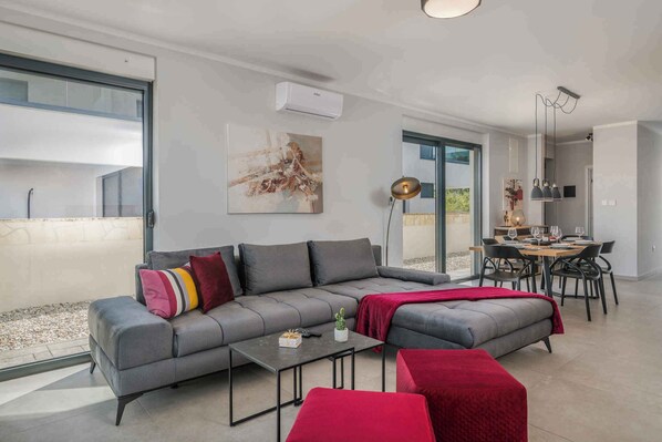 Een moderne woonkamer met een grijze modulaire bank, een kleine salontafel, en een eethoek met een houten tafel en stoelen.