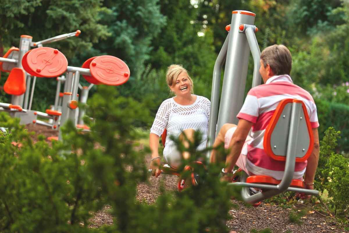 An outdoor gym with exercise equipment, surrounded by greenery.