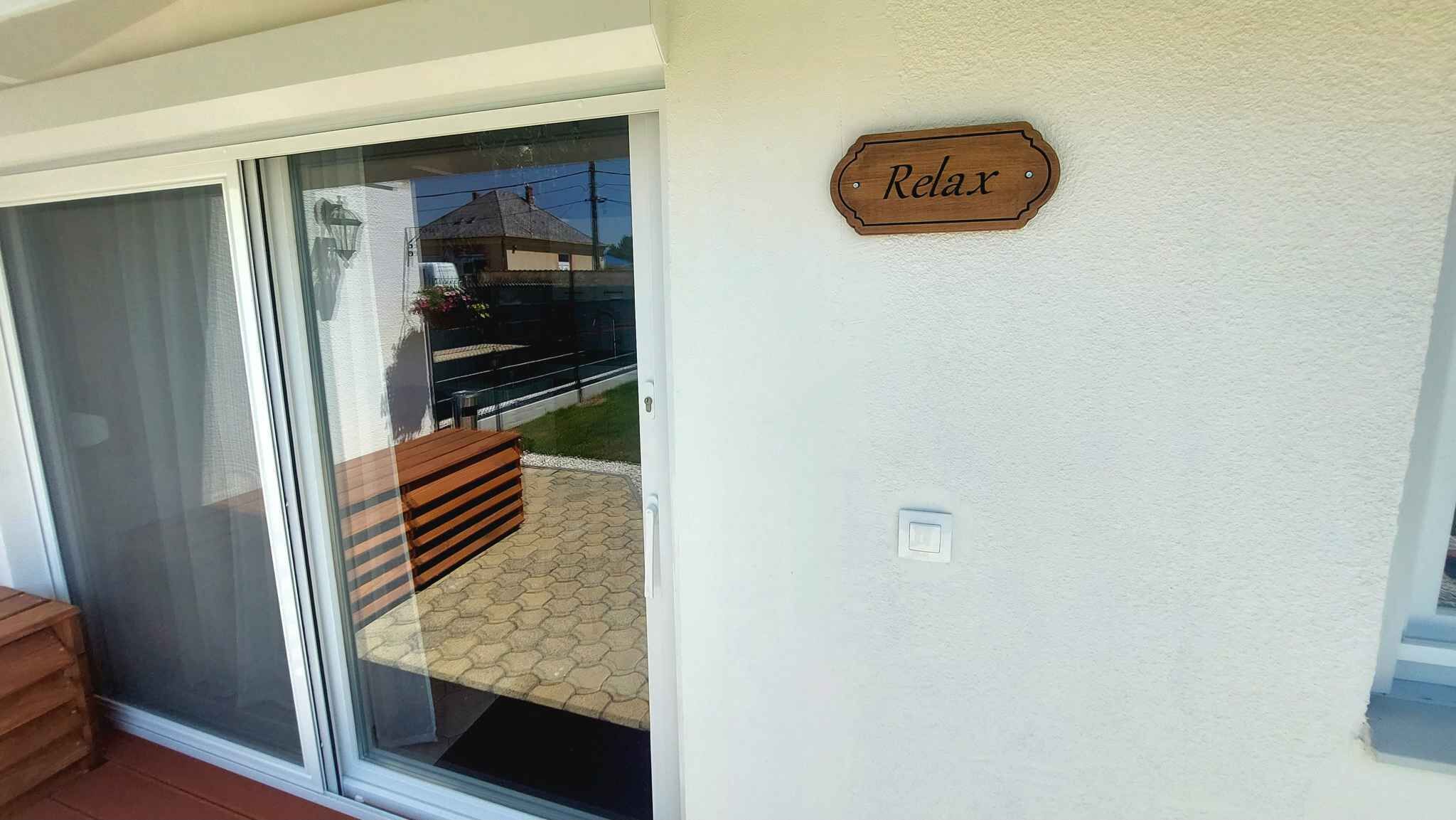 Een glazen schuifdeur die leidt naar een terras met een houten bank en een bord waarop 'Relax' staat.
