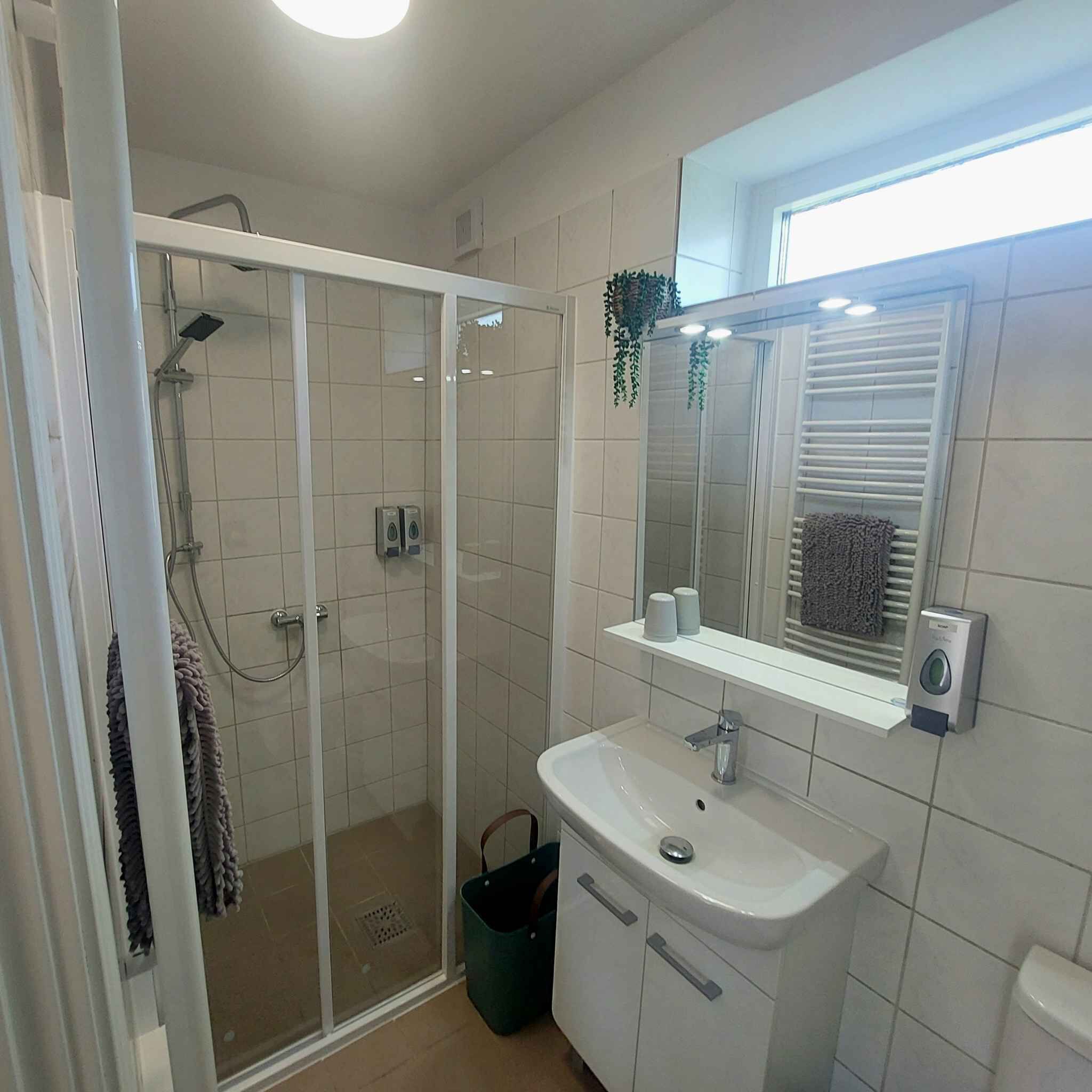 Un baño moderno con cabina de ducha de vidrio, un lavamanos con espejo y un perchero para toallas.