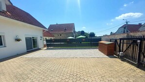 A paved courtyard with a gated entrance, a stone building in the background, and a clear blue sky. - Holiday apartment with terrace and air conditioning (Bük)