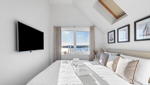 A hotel room with a large bed, a flat-screen TV, a window with curtains, and framed pictures on the wall. - Baltic Sea vacation apartment "Meeresflüstern" with sea view, sauna and close to the beach (Olpenitz)