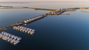 An aerial view of a waterfront property with a long pier extending into the water, featuring multiple docked boats and a row of buildings along the shore. - Baltic Sea vacation apartment "Meeresflüstern" with sea view, sauna and close to the beach (Olpenitz)